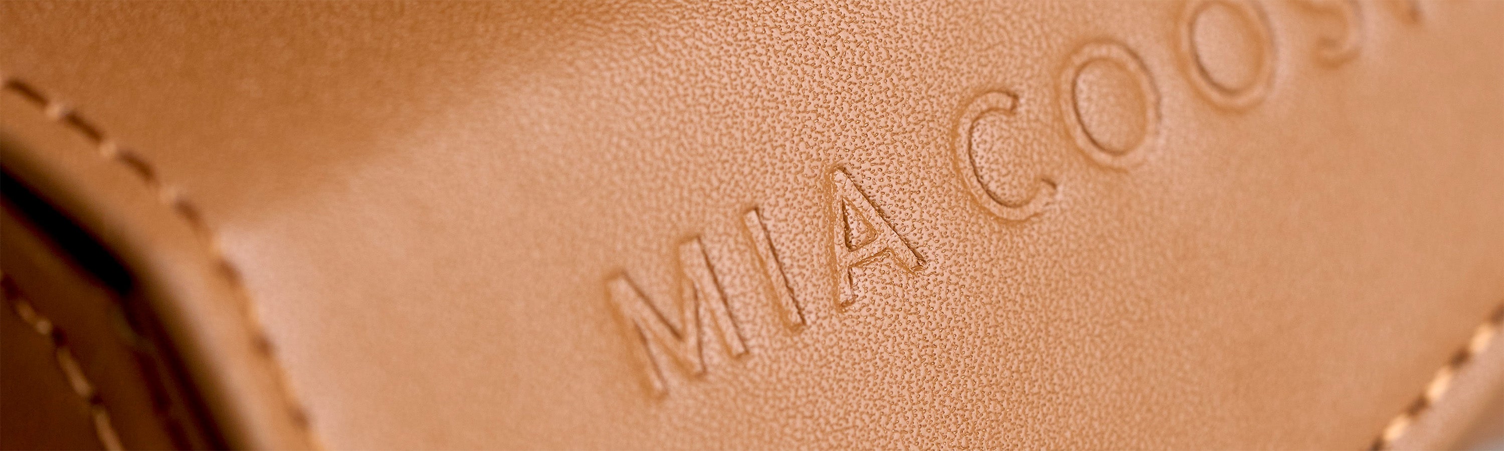 Closeup of Caramel Brown microfibre leather with 'MIA COOSH' embossed logo