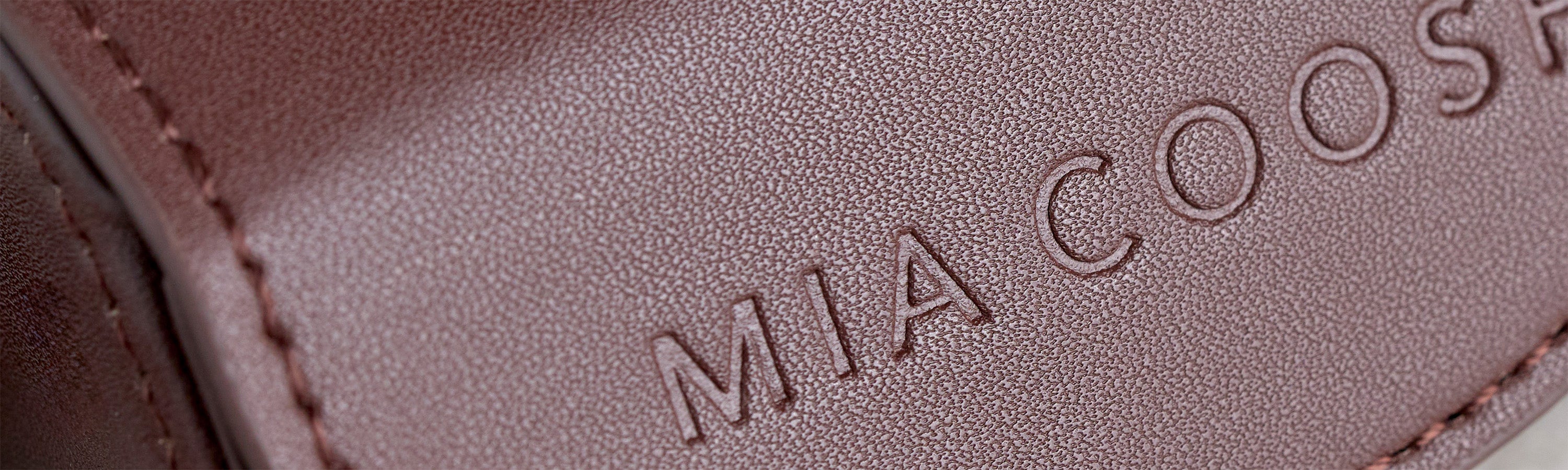 Closeup of Dark Chocolate microfibre leather with 'MIA COOSH' embossed logo